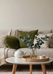 a cozy living room scene with a sofa adorned with pillows and a blanket. A round coffee table holds a tray with a vase of eucalyptus, a teacup, and a teapot.