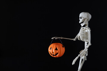 Skeleton holding a bucket of Halloween pumpkins on a black background