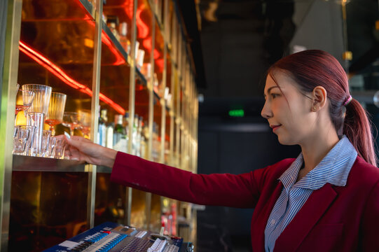Asian bartender woman arranging shot glasses on shelf working behind counter bar
