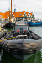 Black inflatable boat moored at a harbor, surrounded by colorful buildings and calm water, showcasing marine life and nautical lifestyle in a serene setting