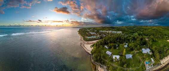 A stunning wide aerial panorama of the Fijian coastline at golden hour. The setting sun illuminates...