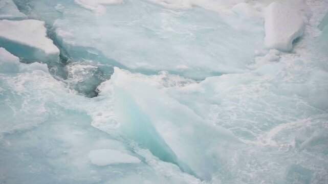 Icebreaking vessel bow pushing through fragmented sea ice and turquoise floes, churning polar water as pressure shatters sheets into slabs and swirling slush in winter light