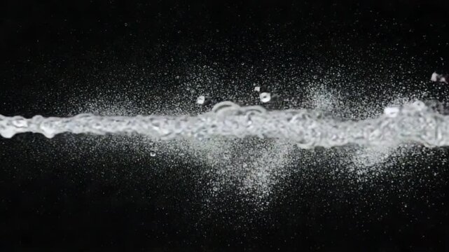 A powerful horizontal jet of clear water splashing and creating droplets against a stark black background.