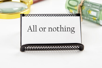 text ALL OR NOTHING on a white business card on a white background in a black stand next to it in...