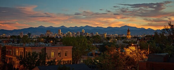 Cityscape view at dusk featuring buildings, trees and mountains under a sky with streaks of orange and pink clouds, showcasing urban beauty