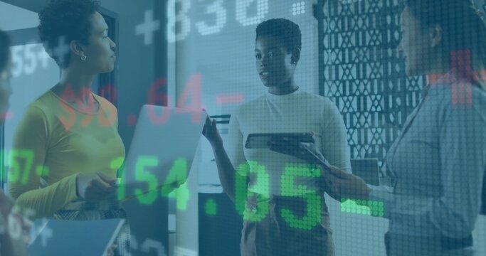 Tablet-holding woman guiding team via stock data overlay in boardroom, with laptop notepad stylus