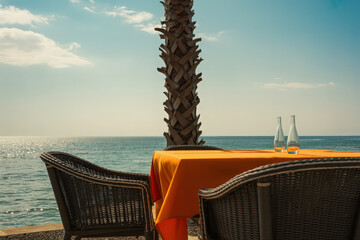 Outdoor dining table with orange cloth and wicker chairs overlooking the ocean on a sunny day view