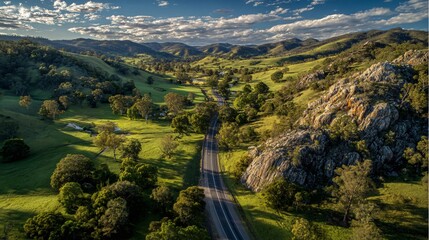 Obraz premium Aerial view displays a winding rural highway through lush green hills and valleys landscape.