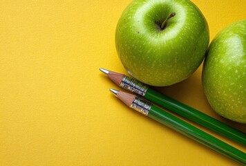 Two green apples rest beside two green pencils against a bright yellow background. Close up, eye level, plenty of negative space