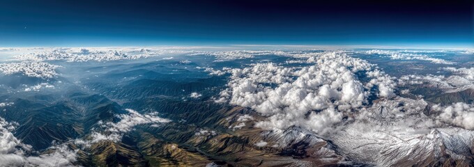 Aerial panorama of mountain range partially covered in clouds under a clear blue sky, capturing a scenic and ethereal landscape