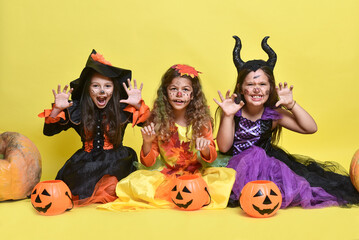 Little girls in Halloween costumes. Children are sitting on a yellow background
