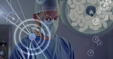 Standing surgeon in scrubs operating in OR, with overhead lamp, monitors and interface overlays