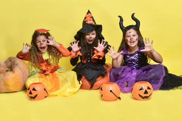 Little girls in Halloween costumes. Children are sitting on a yellow background