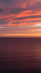 Obraz premium A tranquil seascape at twilight with a dramatic, fiery sky of orange and pink clouds reflecting on the calm, endless ocean