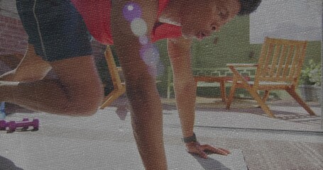 Man wearing red top and sports watch performing pushup on backyard deck, with purple dumbbells