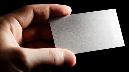 Obraz premium A blank business card is held in a hand against a dark background, highlighting the texture and simple design.