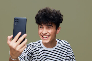 smiling man taking selfie with smartphone, casual striped shirt, curly hair, joyful expression,...