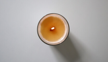 Lit candle in glass holder, shot from top down perspective. Soy candle with wooden wick. Placed in center of white background. Warm glow of flame creates cozy atmosphere, ideal for of relaxation.