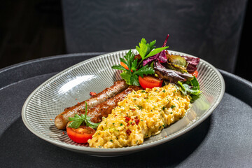 Scrambled eggs with sausages, fresh salad, and tomatoes on a ceramic plate. breakfast