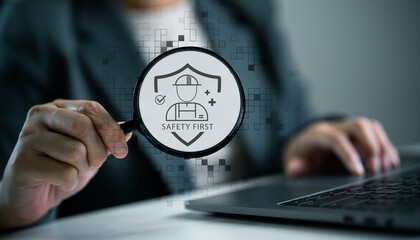 A business person holding a magnifying glass with “Safety First” sign, workplace safety inspection and occupational health standards in the digital age.