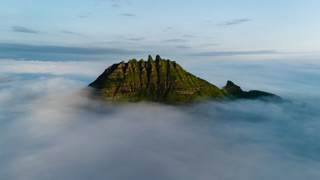 Rugged peaks of a striking mountain emerge from swirling clouds, showcasing the raw beauty of the Faroe Islands. This stunning landscape offers a sense of tranquility and adventure.