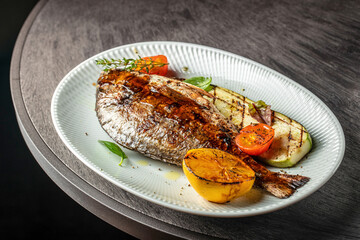 Grilled dorado fish with vegetables and lemon on a plate