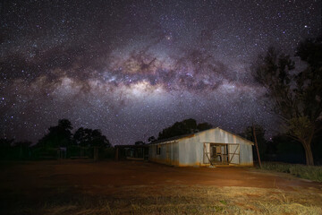 The cosmic dust and the stars of the Milky Way galaxy stretch over the top of a small shearing shed...