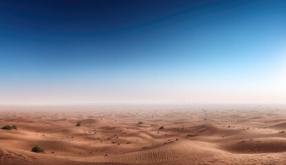Vast desert landscape under a clear, vibrant blue sky, with a hazy, pale layer of mist or fog near the horizon.  Sparse, low vegetation dots the sandy dunes