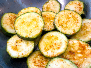 Sliced zucchini with seasoning and oil in bowl, close up view, fresh green vegetable prepared for grilling, roasting, salad or healthy meal.