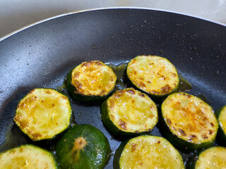 Fried zucchini slices with oil in pan, close up view, golden brown vegetable cooking on stove, healthy vegetarian or vegan meal preparation.