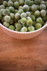 Fresh frozen green peas served in a white bowl on a rustic wooden table, close-up with copy space.