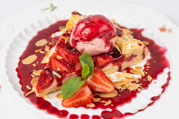 Close-up of a slice of strawberry pie served with a scoop of ice cream and almond flakes on a white background.