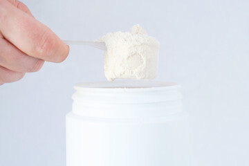 Protein powder in scoop from plastic jar side view on gray background close-up.
