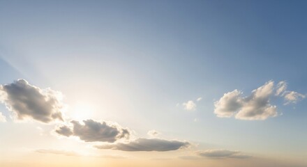 Obraz premium Pale sunlight filters through scattered clouds against a serene pale blue sky