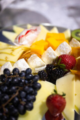 Elegant cheese board with assorted cheeses, fresh grapes, strawberries, blackberries, pineapple, mango, and kiwi - perfect for parties, gatherings, or gourmet appetizers.
