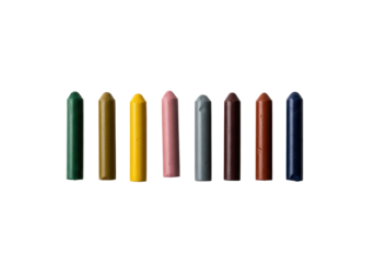 A top-down shot of 7-9 well-used, stubby wax crayons in muted earthy colors, loosely arranged on a transparent background with soft light and copy space. Contemplative art tools concept