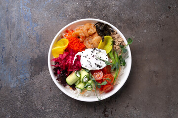 Fresh poke bowl with rice, grilled shrimp, avocado, cucumber, tomatoes, red cabbage, and sour cream - vibrant, healthy meal on a rustic background.