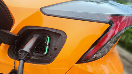 Fototapeta premium close-up view of an orange electric car charging at a modern station in a shopping mall parking area during daytime, focusing on the charging head as a symbol of renewable energy