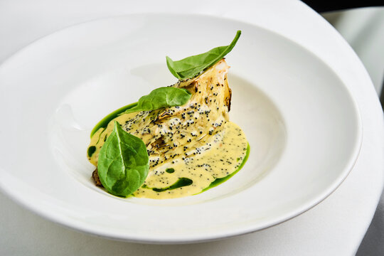 Whole roasted celeriac is plated beautifully, topped with a savory tahini herb sauce and garnished with tobiko and fresh greens. This dish showcases a blend of flavors and textures