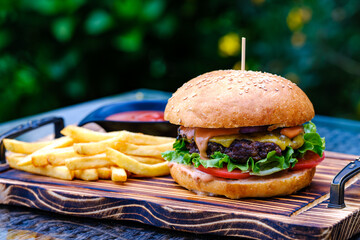 A freshly prepared cheeseburger served with crispy french fries and ketchup on a wooden serving...