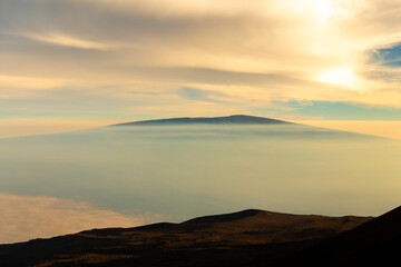 Sunset view from the summit of Mauna Kea on the Big Island of Hawaii, with volcanic slopes and clouds glowing in golden light.
