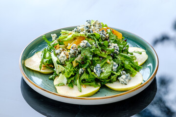 A vibrant green salad featuring fresh lettuce, sliced apples, blue cheese crumbles, and nuts, served on a ceramic plate