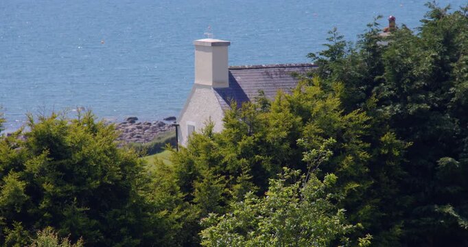 Wide shot of a Gable end of a cottage with trees and wood in foreground at Criccieth