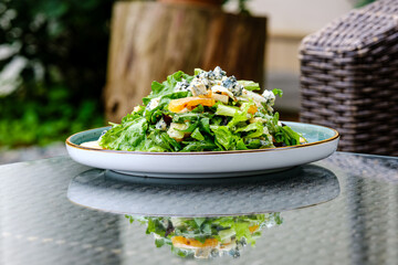 A vibrant green salad featuring fresh lettuce, sliced apples, blue cheese crumbles, and nuts, served on a ceramic plate