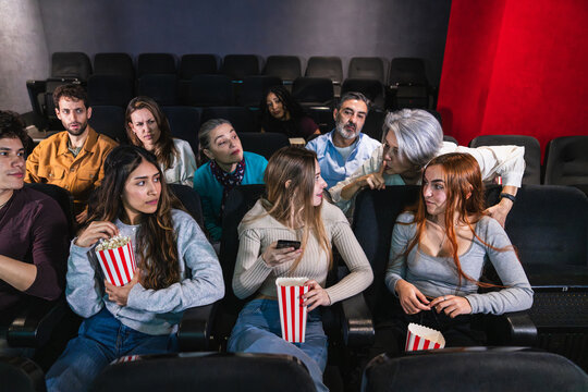People are getting annoyed by woman using smartphone during film projection in crowded movie theater and an woman asks him to be quiet