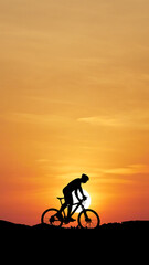 Silhouette of a Mountain Biker: A mountain biker pedals against a vibrant orange sky, silhouetted by the sun, offering a serene view, conveying the thrill of outdoor adventure.