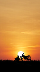 Golden Hour of Freedom: A solitary silhouette of a person rests beside their off-road motorcycle, a symbol of adventure, under a breathtaking sunset. Capturing a moment of contemplation and freedom.