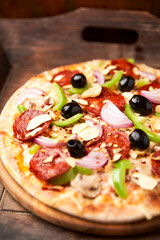 Pizza with chorizo ​​sausage, mozzarella cheese, green pepper and black olives. Rustic wooden background. Soft focus.	