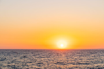 Beautiful view of a summer sunset over the sea horizon. The glowing sun creates golden reflections on the water, filling the sky with warm orange and yellow tones. Symbol of calmness, romance