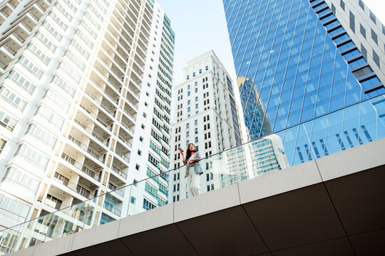 Low-angle view of modern skyscrapers with glass facades and a pedestrian sky bridge, showcasing contemporary urban architecture and corporate office towers against a bright sky. - Powered by Adobe